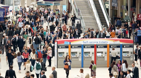 Crowded train station with people and self-service ticket machines.