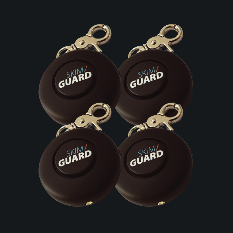 Four Skimguard Personal Alarms with front buttons and attached metal clips, shown overlapping.